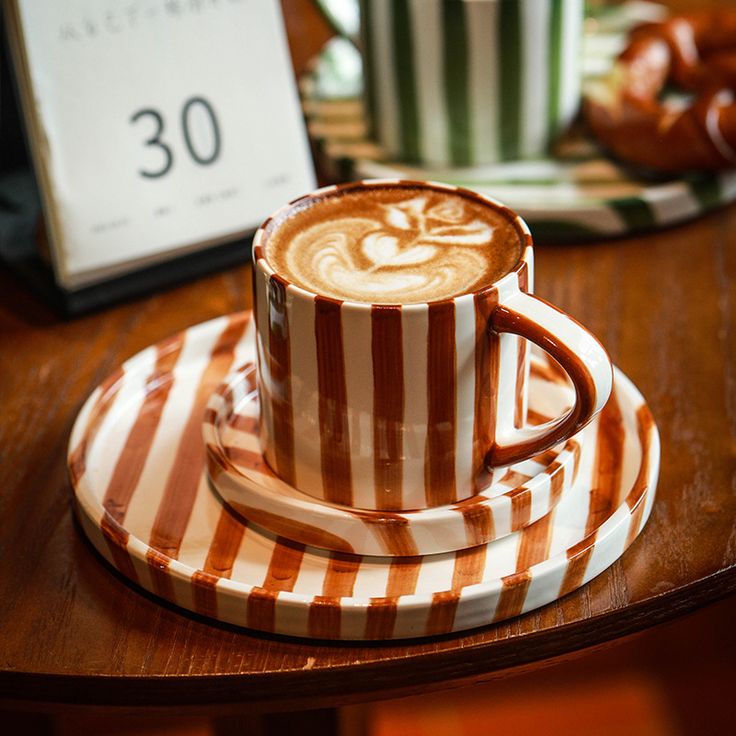 Striped coffee mug with latte art on a matching saucer.