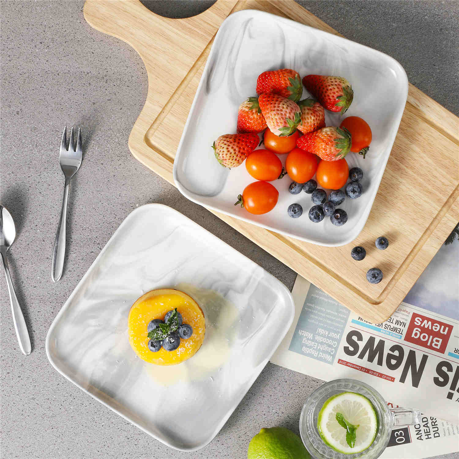 Two marble-pattern square porcelain dessert plates with a mini cheesecake, strawberries, blueberries, and cherry tomatoes