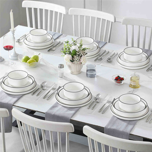 Elegant white dining table set with minimalist black-rimmed dinnerware and floral centerpiece.