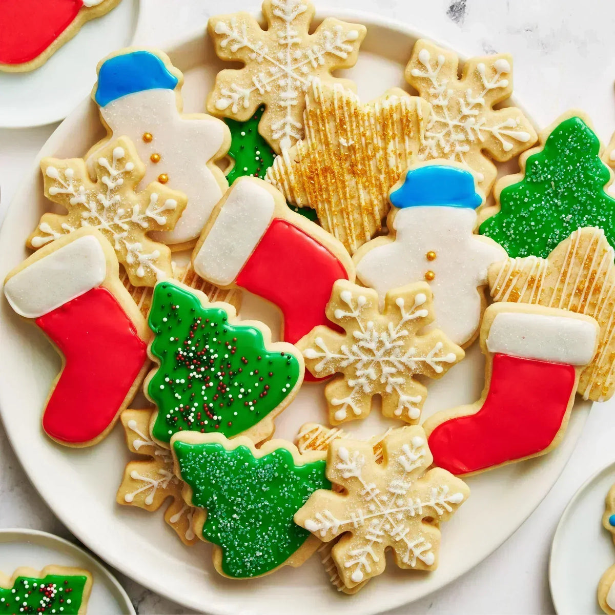 Royal icing Christmas cookies in snowflake, tree, stocking, and snowman shapes on a white plate