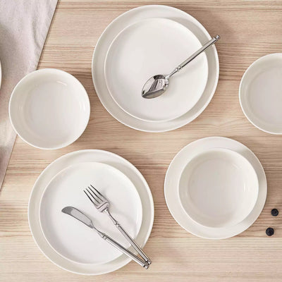 MINA porcelain dinnerware set featuring curved-edge plates and bowls with lifted rims.#color_ivory-white