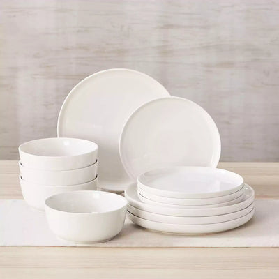 MINA porcelain dinnerware set featuring curved-edge plates and bowls with lifted rims.#color_ivory-white