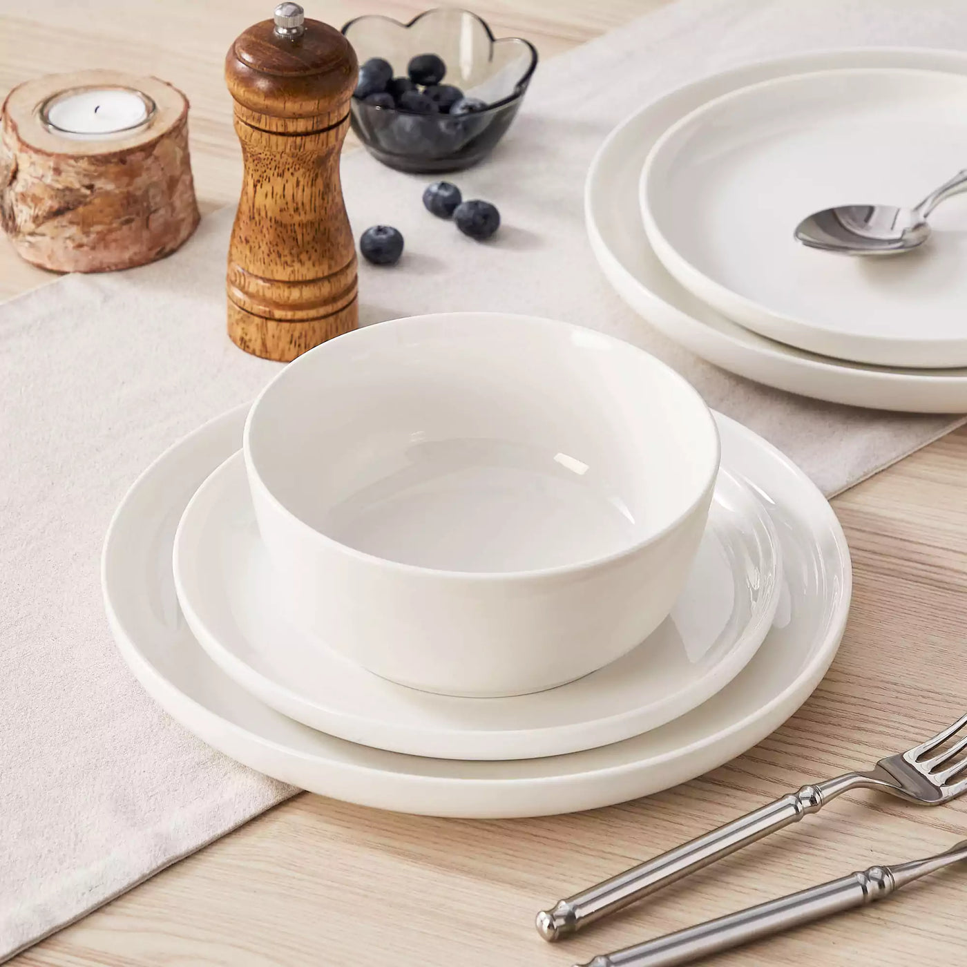 MINA porcelain dinnerware set featuring curved-edge plates and bowls with lifted rims.#color_ivory-white