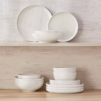 MINA porcelain dinnerware set featuring curved-edge plates and bowls with lifted rims.#color_ivory-white