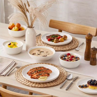 MINA porcelain dinnerware set featuring curved-edge plates and bowls with lifted rims.#color_ivory-white