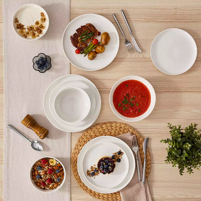 MINA porcelain dinnerware set featuring curved-edge plates and bowls with lifted rims.#color_ivory-white