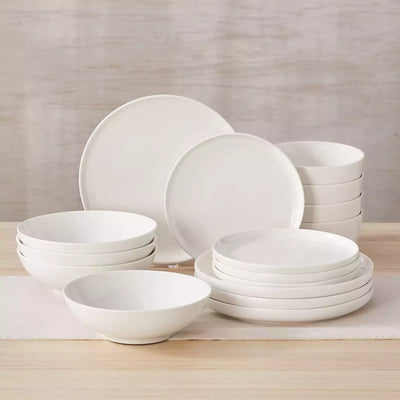MINA porcelain dinnerware set featuring curved-edge plates and bowls with lifted rims.#color_ivory-white