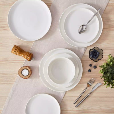 MINA porcelain dinnerware set featuring curved-edge plates and bowls with lifted rims.#color_ivory-white