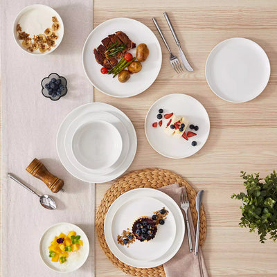 MINA porcelain dinnerware set featuring curved-edge plates and bowls with lifted rims.#color_ivory-white