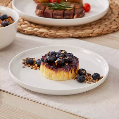 MINA porcelain dinnerware set featuring curved-edge plates and bowls with lifted rims.#color_ivory-white