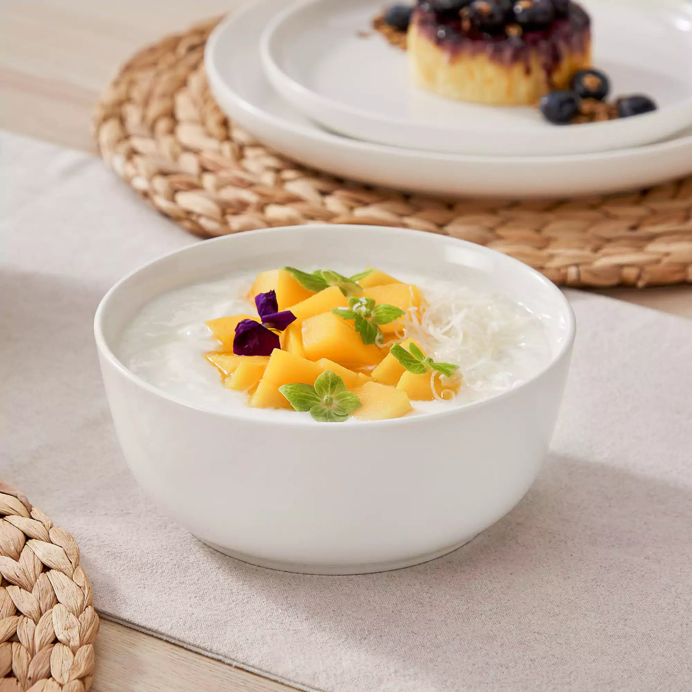 MINA porcelain dinnerware set featuring curved-edge plates and bowls with lifted rims.#color_ivory-white