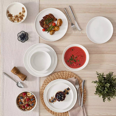 MINA porcelain dinnerware set featuring curved-edge plates and bowls with lifted rims.#color_ivory-white