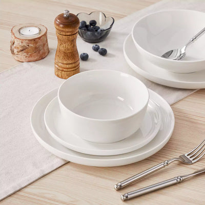 MINA porcelain dinnerware set featuring curved-edge plates and bowls with lifted rims.#color_ivory-white