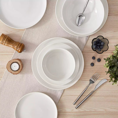 MINA porcelain dinnerware set featuring curved-edge plates and bowls with lifted rims.#color_ivory-white